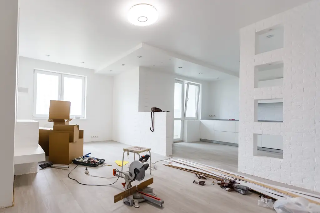 Renovierung Heller, leerer Raum mit weißen Wänden und Decke, mehreren Kartons, einer Kappsäge auf dem Boden und verstreuten Werkzeugen