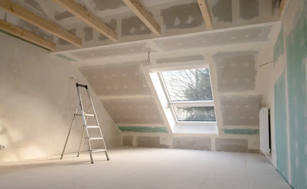 Trockenbau-Dach Innenraum eines Dachgeschosses mit Trockenbauwänden und -decken, einer Leiter und einem großen Dachfenster