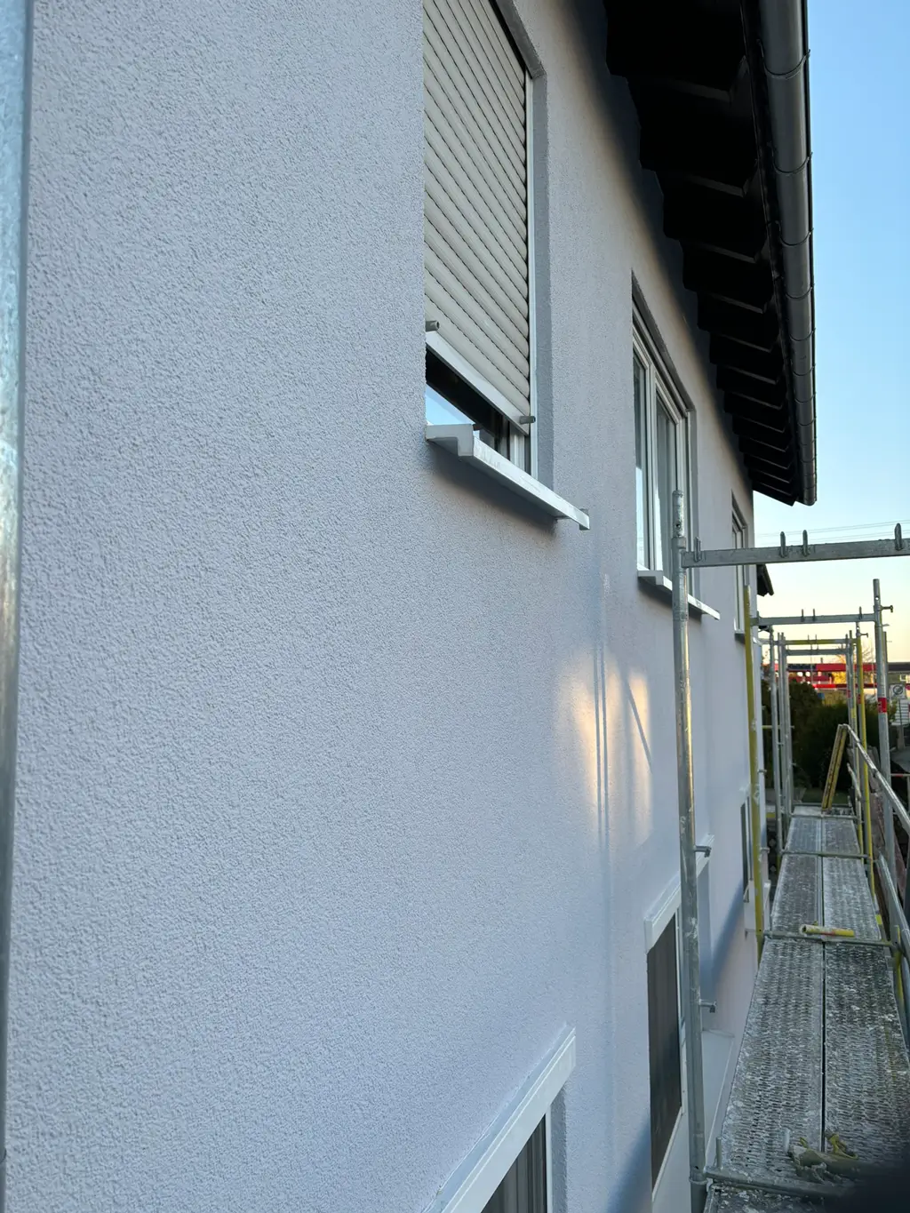 Fassade eines Hauses mit glatter Putzoberfläche und eingerüstetem Gerüst an der Seite