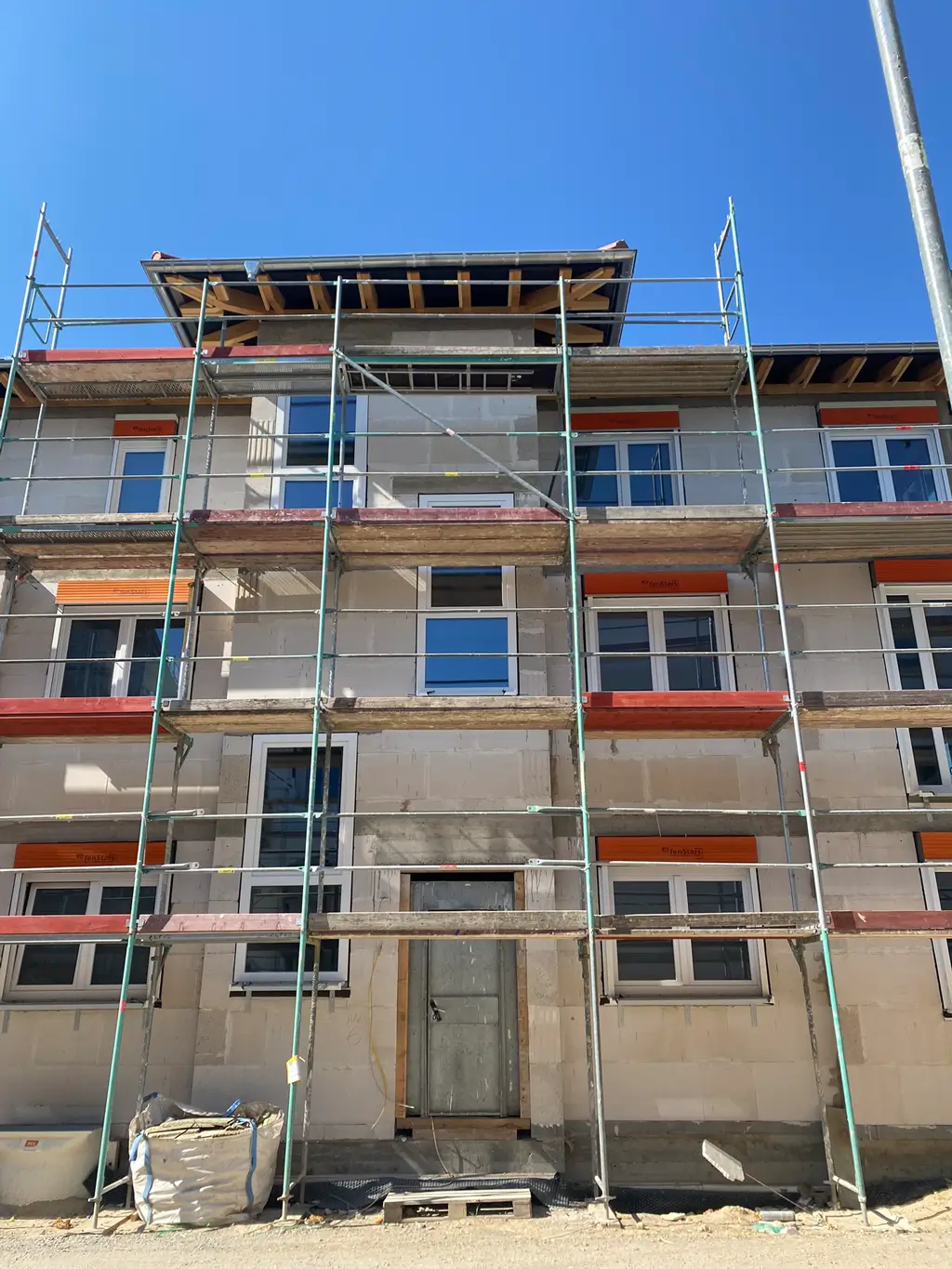 Mehrstöckiges Gebäude mit Gerüst vor der Fassade und klarem Himmel im Hintergrund