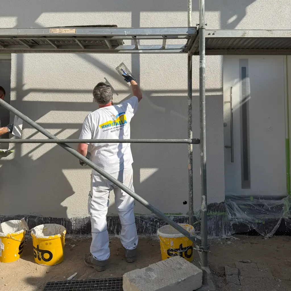 Fassaden verputzen Mann in weißer Arbeitskleidung streicht Fassade mit Spachtel auf Gerüst vor Hauswand