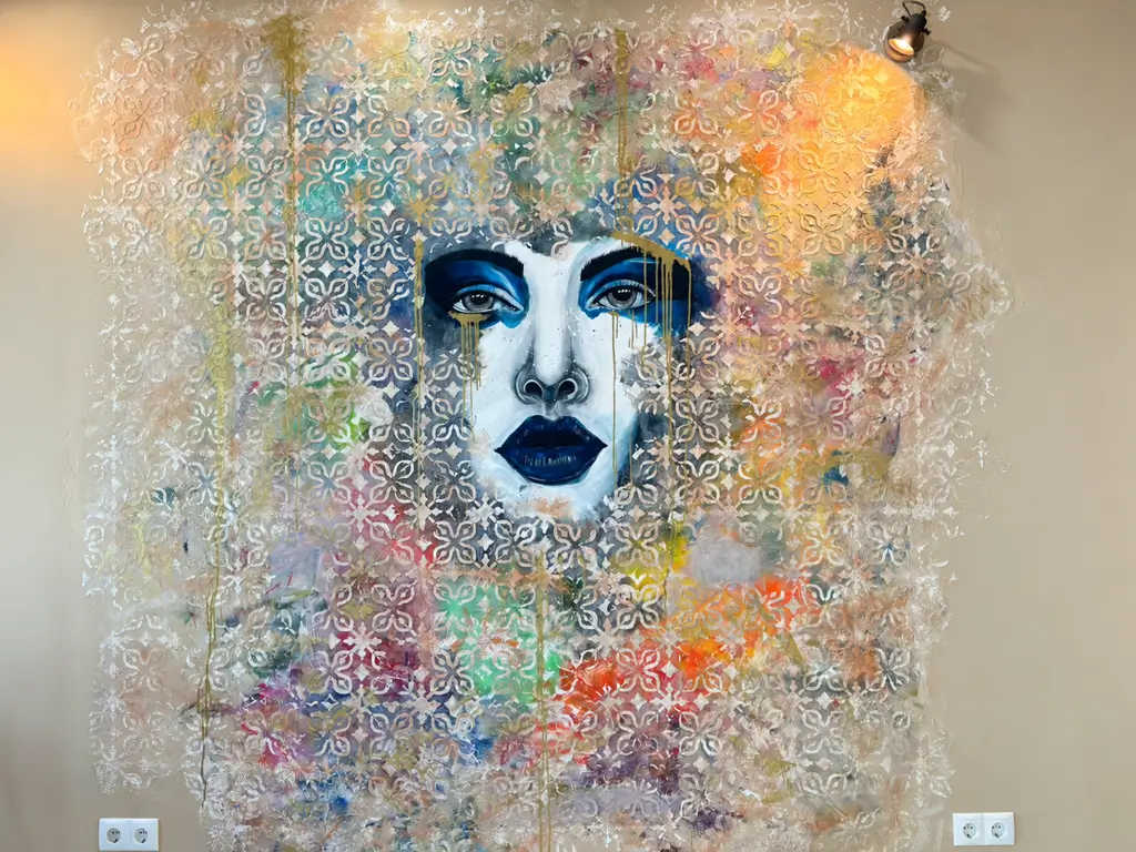Gesicht einer Frau mit dunklem Lippenstift und blauen Augen in einem farbenfrohen Wandgemälde mit floralen Mustern