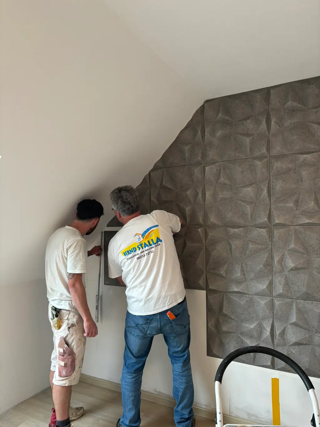 Zwei Männer montieren dreidimensionale Schallschutzplatten an einer Wand