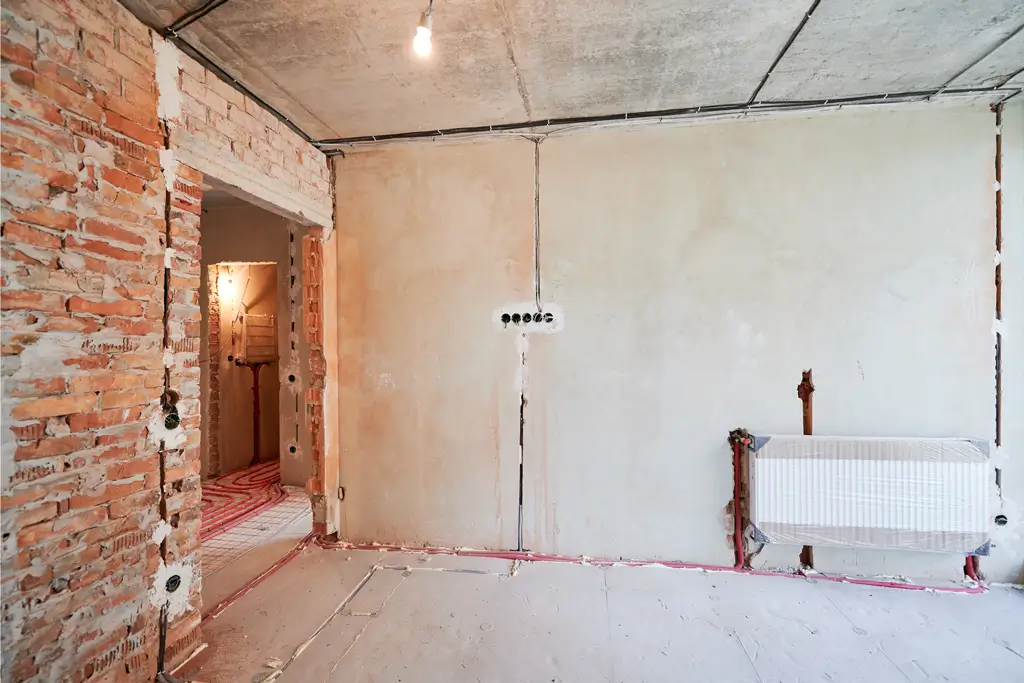 Vorher Sanierung Raum Rohbau eines Raums mit unverputzten Ziegelwänden, unvollständiger Elektroinstallation und Heizkörper an der Wand